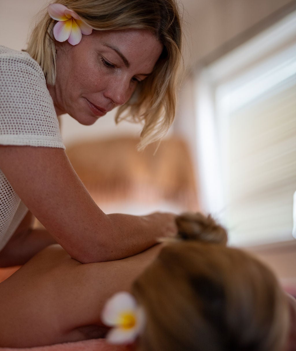 Jodie working on a client's shoulders, a frangipani in the client's hair